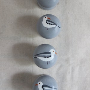 K&ouml;nnte beinhalten: Vier graue runde Ornamente mit gemalten M&ouml;wen. Jedes Ornament zeigt eine wei&szlig;e M&ouml;we mit schwarzen Markierungen und einem orangefarbenen Schnabel.
