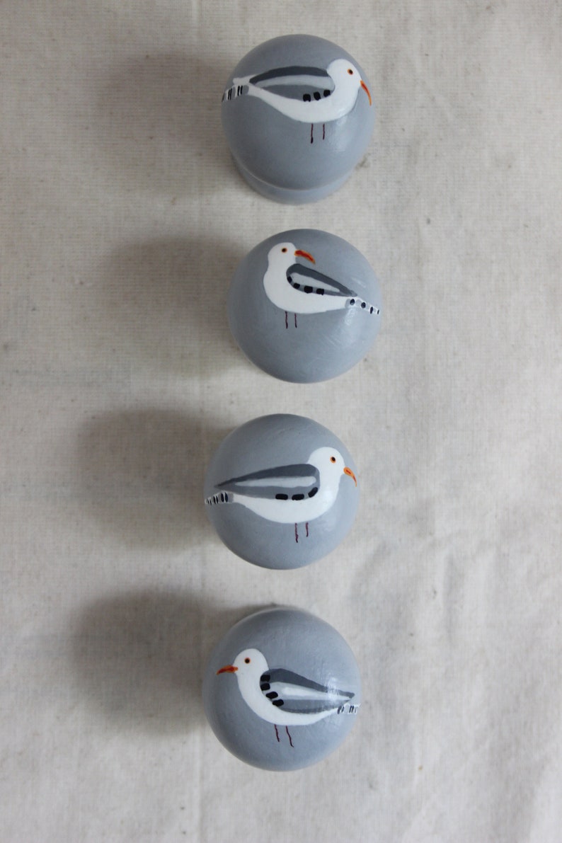 K&ouml;nnte beinhalten: Vier graue runde Ornamente mit gemalten M&ouml;wen. Jedes Ornament zeigt eine wei&szlig;e M&ouml;we mit schwarzen Markierungen und einem orangefarbenen Schnabel.