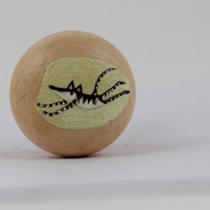 Pode incluir: Objeto decorativo esf&eacute;rico bege com uma ilustra&ccedil;&atilde;o pintada de um animal a correr. O animal &eacute; preto e branco com um focinho comprido e corpo listrado, sobre um oval verde claro.