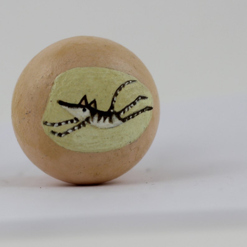 Pode incluir: Objeto decorativo esf&eacute;rico bege com uma ilustra&ccedil;&atilde;o pintada de um animal a correr. O animal &eacute; preto e branco com um focinho comprido e corpo listrado, sobre um oval verde claro.