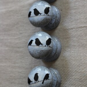 K&ouml;nnte beinhalten: Sechs blaue Keramik-Kn&ouml;pfe mit wei&szlig;er Waschung. Jeder Knopf zeigt eine Silhouette von drei V&ouml;geln, die auf einem Draht sitzen.