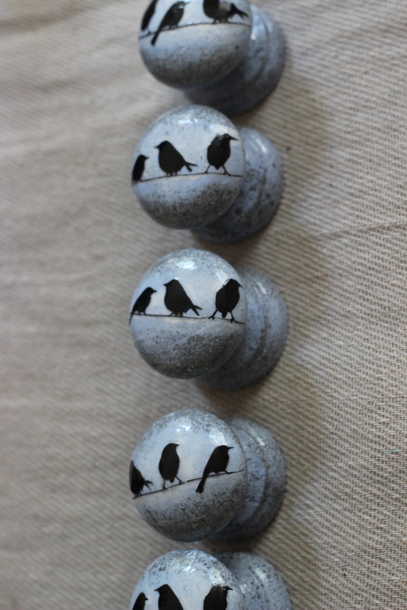 K&ouml;nnte beinhalten: Sechs blaue Keramik-Kn&ouml;pfe mit wei&szlig;er Waschung. Jeder Knopf zeigt eine Silhouette von drei V&ouml;geln, die auf einem Draht sitzen.