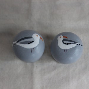 K&ouml;nnte beinhalten: Zwei runde, graue Keramikornamente mit bemalten M&ouml;wenmotiven. Die M&ouml;wen sind wei&szlig; mit schwarzen Markierungen und orangefarbenen Schn&auml;beln.