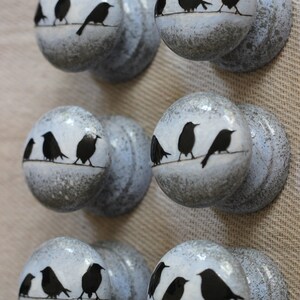 K&ouml;nnte beinhalten: Sechs graue Keramikkn&ouml;pfe mit wei&szlig;em Hintergrund und schwarzen Silhouetten von V&ouml;geln auf einem Draht. Die Kn&ouml;pfe haben eine gesprenkelte Oberfl&auml;che.