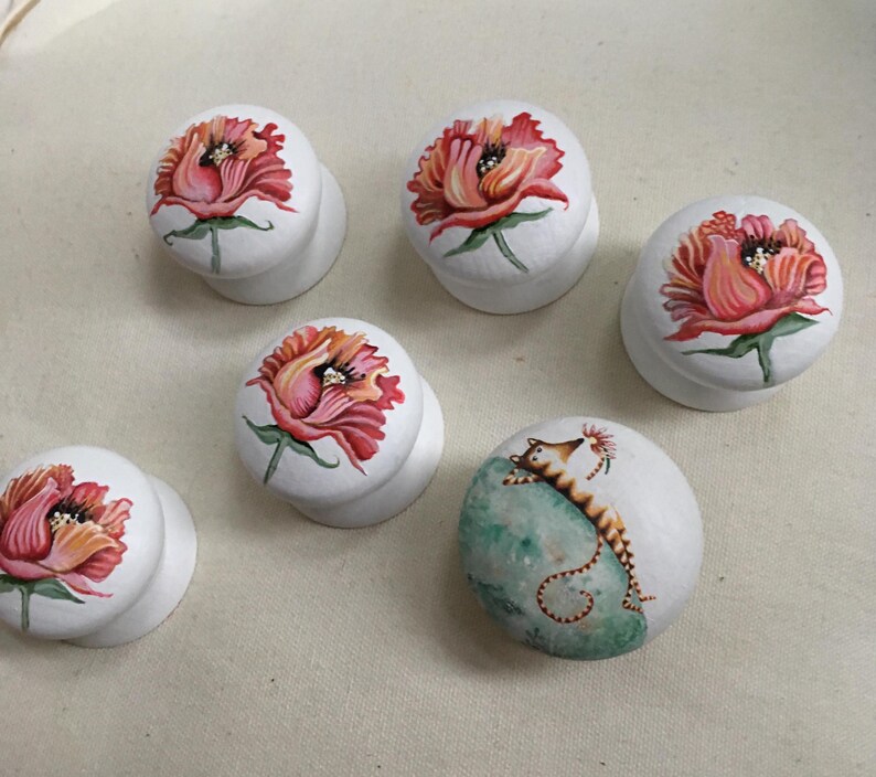 Puede incluir: Pomos de armario blancos con dise&ntilde;os florales pintados a mano en tonos rojos, rosas y naranjas. Un pomo presenta un dise&ntilde;o de caballito de mar sobre un fondo turquesa. Estos pomos decorativos a&ntilde;aden un toque art&iacute;stico a los muebles.