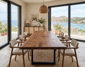 Puede incluir: Un comedor con una gran mesa rectangular de madera con veta natural y base de metal negro, rodeada de seis sillas tapizadas de colores claros con marcos de madera, sobre una alfombra tejida en una habitación con grandes ventanales.