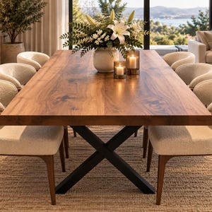 May include: A rectangular wooden dining table with a natural grain finish and a black metal X-shaped base. Six chairs with curved wooden frames and cream-colored textured upholstery surround the table. A vase with white lilies sits in the center.