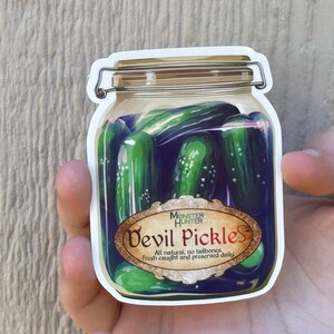 Puede incluir: Una pegatina de un frasco de vidrio lleno de pepinillos verdes. El frasco tiene una etiqueta que dice "Monster Hunter Devil Pickles" y "All natural, no tailbones, fresh caught and preserved daily."