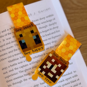 May include: Four yellow and brown bookmarks with a honeycomb pattern and a pixelated bee design. Each bookmark has a different phrase: "Bee Sweet", "Bee Happy", "Bee Free", and "Bee Busy".