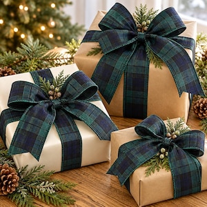 May include: Three square gift boxes wrapped in plain brown and white paper, each adorned with a large, dark green and navy blue plaid fabric bow, accented with small sprigs of evergreen needles and tiny light-colored decorative berries.