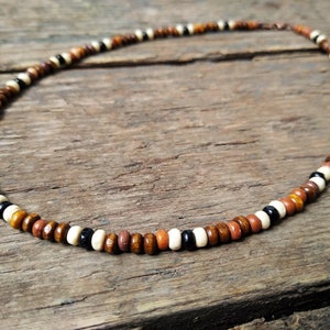 Necklace made from small wooden beads approx. 3 or 4mm in diameter. The beads are arranged 5 brown beads, 1 white bead, 1 black bead then another white bead. This pattern is then repeated. Fastened with an antique copper effect  lobster clasp.