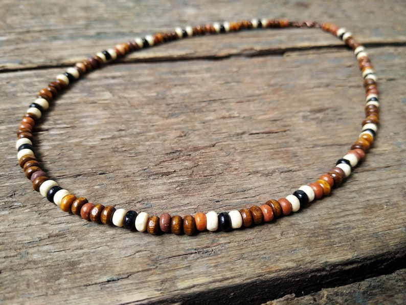 Necklace made from small wooden beads approx. 3 or 4mm in diameter. The beads are arranged 5 brown beads, 1 white bead, 1 black bead then another white bead. This pattern is then repeated. Fastened with an antique copper effect  lobster clasp.