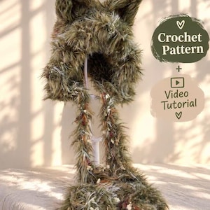 Puede incluir: Una capucha de color verde oliva con orejas de gato hecha de hilo texturizado con largas solapas colgantes. La capucha presenta detalles de hilo blanco y marrón. El texto a la derecha dice Crochet Pattern + Video Tutorial con corazones.