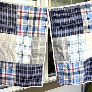 May include: Two patchwork quilts, each with a unique arrangement of plaid fabric squares in navy, red, blue, and beige. The quilts are hanging from a clothesline, showcasing their handmade design.
