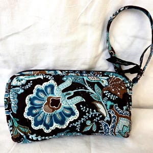 May include: A rectangular, floral-patterned wallet with a matching strap. The wallet features a dark brown background with blue, teal, and white floral designs. The strap is attached to the top of the wallet with a black ribbon.