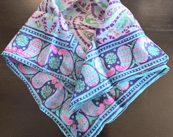 May include: A square scarf featuring a vibrant paisley pattern in shades of bright pink, light blue, dark purple, and green. The design includes a central floral motif surrounded by a wide border of repeating paisley shapes and small flower accents.