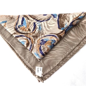 May include: Folded silk scarf with a layered design. The top layer features a pattern of blue, brown, and beige swirls, while the bottom layer has a beige zebra stripe pattern. The scarf is folded into a triangle shape.