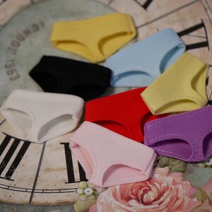May include: Assortment of colorful underwear in various colors, including yellow, black, blue, red, pink, and purple. The underwear is arranged on a vintage clock face.