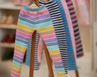 Könnte beinhalten: Ein Satz bunter, gestreifter Leggings, die an einem Holzgestell hängen. Die Leggings sind in verschiedenen Farben, darunter rosa, blau, gelb und weiß.