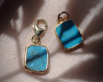 May include: Two gold charms with turquoise stones. The charms are rectangular and have a slightly irregular shape. The stones are a vibrant blue color.