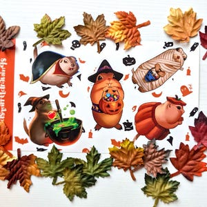 May include: A sticker sheet featuring five cartoon squirrels in Halloween costumes, including a vampire, a witch with a cauldron, a wizard with a pumpkin bucket, a mummy, and a pumpkin. The sheet includes small orange icons of bats and ghosts.
