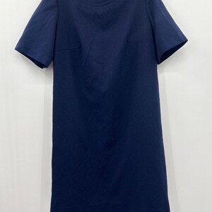 May include: A solid navy blue shift dress featuring short sleeves, a round neckline with subtle horizontal stitched detailing, and a straight hemline. The garment includes a visible vertical zipper closure at the center of the upper back.