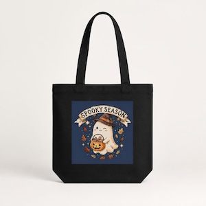 Peut inclure: Un sac fourre-tout noir avec un motif central sur fond bleu foncé. L'illustration représente un fantôme blanc portant un chapeau de sorcière, tenant un seau citrouille rempli de bonbons, entouré de feuilles d'automne et du texte SPOOKY SEASON.