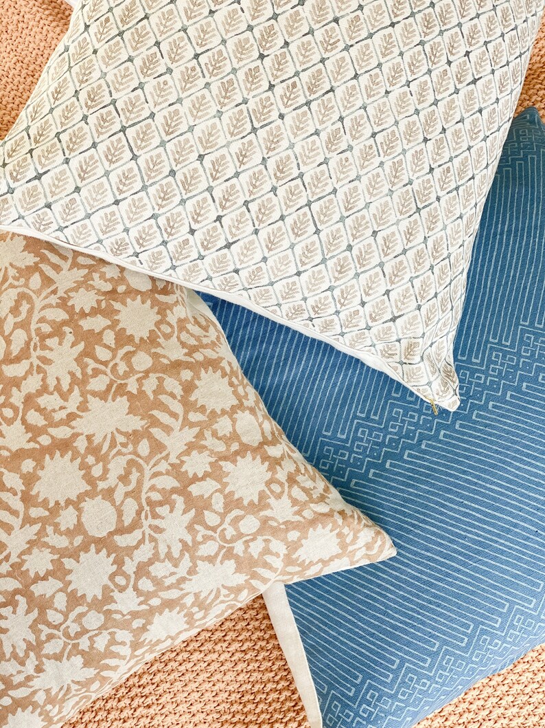 May include: Three decorative throw pillows with different patterns. The top pillow has a white background with a repeating pattern of small brown leaves. The middle pillow has a tan background with a repeating pattern of white flowers. The bottom pillow has a blue background with a repeating pattern of white geometric shapes.