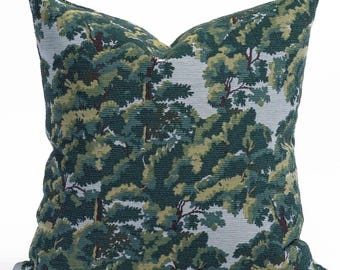 May include: Square throw pillow with a forest scene design. The pillow features a repeating pattern of trees in shades of green, brown, and yellow against a light blue background. The pillow is made of a textured fabric.