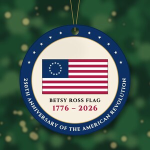 May include: A round, flat ornament featuring the Betsy Ross flag in the center. The text reads: BETSY ROSS FLAG 1776 - 2026 250TH ANNIVERSARY OF THE AMERICAN REVOLUTION. The border is dark blue with white stars and a gold inner ring.