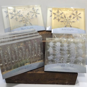 May include: A collection of Hallmark Frostlight Fancies holiday ornaments in clear plastic packaging. Includes two sets of beaded snowflake ornaments, a set of clear glass-like glistening icicles, and a strand of snowflake garland.