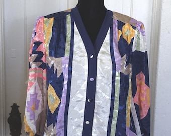 Op de afbeelding: Een blouse met lange mouwen en knoopsluiting met een veelkleurig geometrisch patroon in marineblauw, wit, roze, geel en lavendel. Het kledingstuk heeft een V-hals en effen marineblauwe biezen langs de knoopsluiting, de manchetten en de zoom.