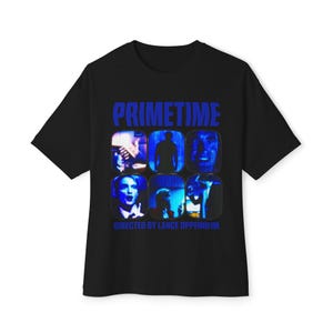 Op de afbeelding: Een zwart t-shirt met korte mouwen met de blauwe tekst PRIMETIME bovenaan en DIRECTED BY LANCE OPPENHEIM onderaan. De centrale afbeelding toont zes rechthoekige panelen in blauwtinten met diverse scènes van mensen.