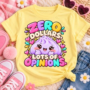 May include: A light yellow t-shirt featuring a central graphic of a smiling purple dumpling character surrounded by colourful hearts and stars. The text "ZERO DOLLARS" appears in bubble letters above the character, and "LOTS OF OPINIONS" below.