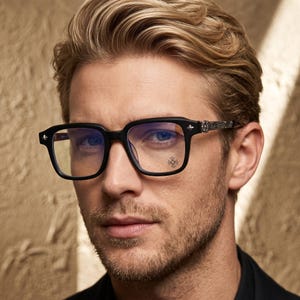 May include: Black rectangular eyeglasses featuring thick frames and silver-toned metal temples with intricate engraved detailing. The lenses are clear with a subtle blue light filter tint and a small circular cross emblem printed on the right lens.