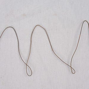 May include: A thin, flexible brown wire stringer featuring a metal swivel and a clip fastener at each end. The wire is bent into a series of loose, undulating loops, with the ends twisted securely around the metal hardware components.