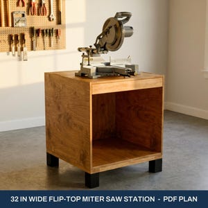 May include: A wooden flip-top miter saw station with a natural wood grain finish, featuring a large open storage compartment and four black square legs. A gray miter saw is mounted on the top surface. Text reads: 32 IN WIDE FLIP-TOP MITER SAW STATION - PDF PLAN.