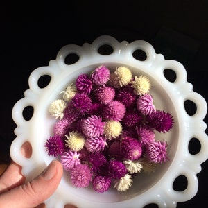 May include: A white ceramic bowl with a scalloped edge, filled with a variety of dried purple and white flowers.