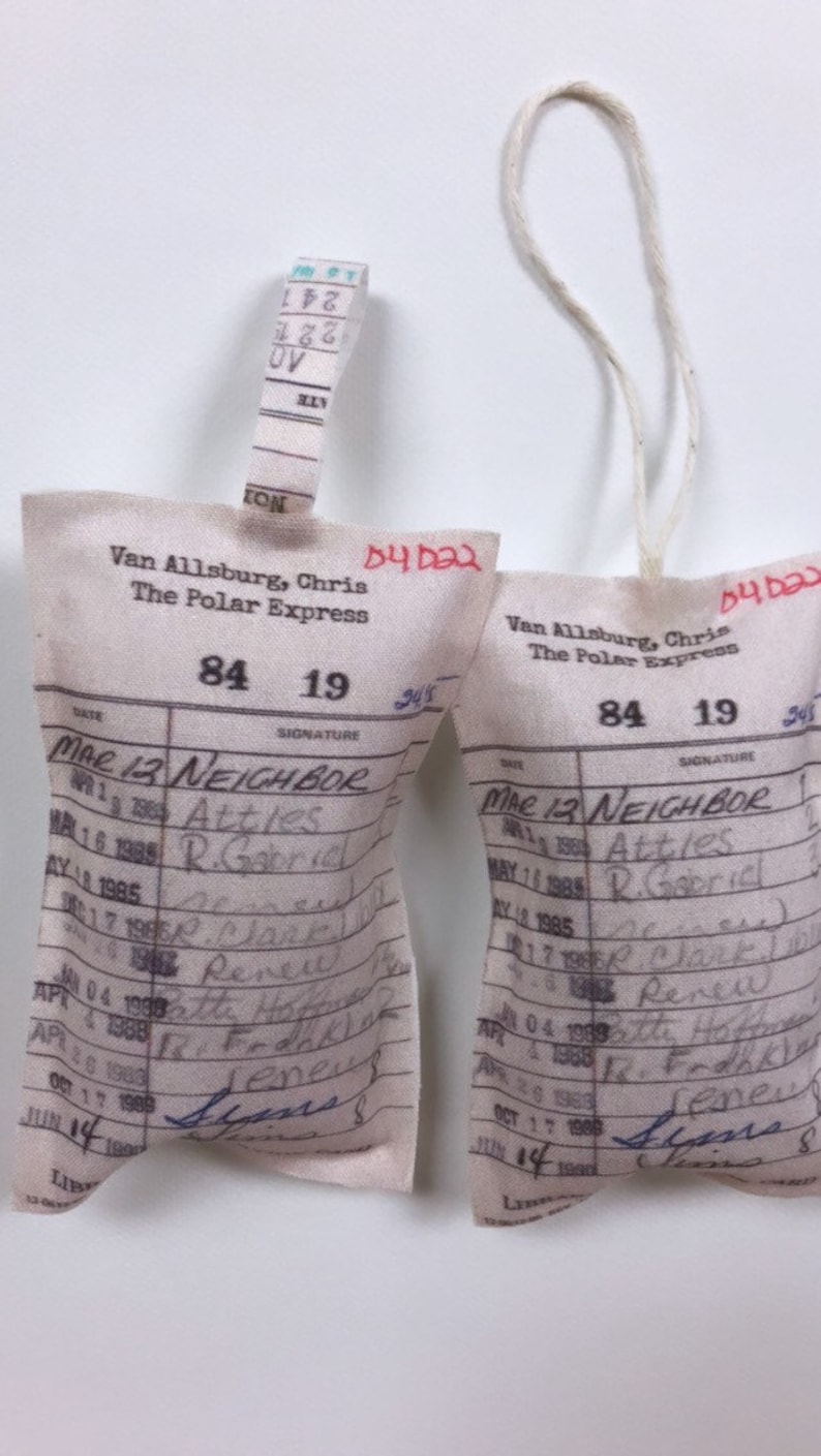 May include: Two white fabric book card pockets with blue handwritten text. The text includes the title "The Polar Express" and the date "Mar 12 Neighbor".