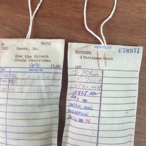 May include: Two vintage library checkout cards, one for "How the Grinch Stole Christmas" by Dr. Seuss and the other for "A Christmas Carol" by Dickens. Both cards have handwritten check-out information and dates.