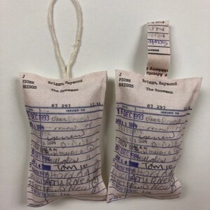 May include: Two white fabric pouches with blue text and handwritten notes. The pouches are labeled "Briggs, Raymond The Snowman" and have a date of December 1993. The pouches are tied with twine.