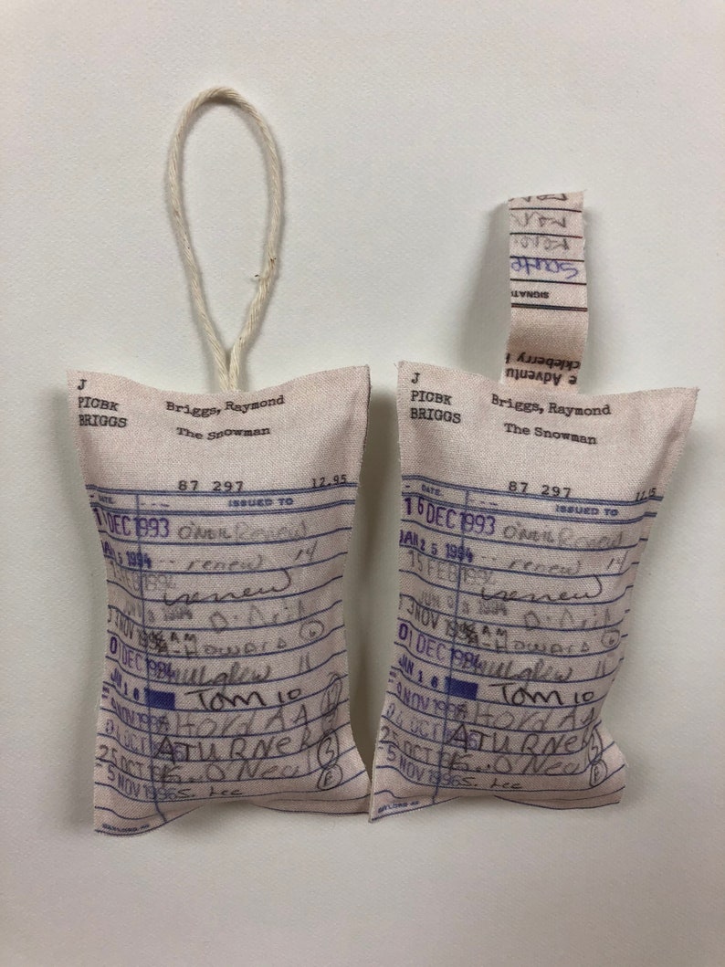 May include: Two white fabric pouches with blue text and handwritten notes. The pouches are labeled "Briggs, Raymond The Snowman" and have a date of December 1993. The pouches are tied with twine.