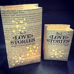 May include: Two brown paper lanterns with white text that reads "Love Stories" and "Love Stories" with a red heart symbol in each. The lanterns are lit with a warm yellow glow.
