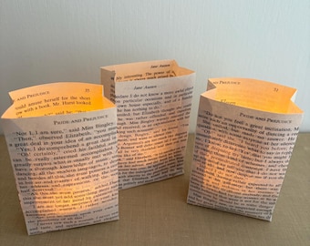 May include: Three handmade paper lanterns, each crafted from pages of "Pride and Prejudice" by Jane Austen. The lanterns are rectangular, with the text visible, and emit a warm, inviting glow. A unique literary-themed home decor item.