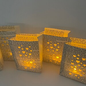 May include: A collection of small paper bags with cut-out hearts and a warm glow emanating from inside. The bags are filled with text from a book, and the text is visible through the cut-out hearts. The bags are arranged in a row on a white surface.