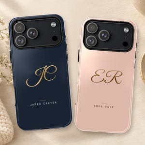 May include: Two smartphone cases, one dark navy blue and one light pink, each featuring a black camera module. The navy case displays gold script initials JC and the text JAMES CARTER. The pink case shows gold script initials ER and EMMA ROSE.