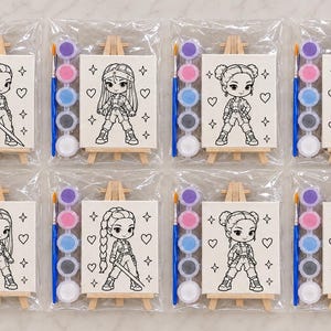 May include: Eight individual craft kits, each sealed in clear plastic, containing a small wooden easel, a white canvas with a black line art illustration of a character, a blue paintbrush, and a strip of five small paint pots in various colours.