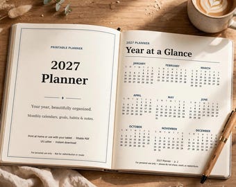Puede incluir: Una agenda 2027 abierta con una página de color crema que muestra un calendario anual Year at a Glance para los doce meses. La página izquierda muestra el título 2027 Planner y texto sobre calendarios mensuales, objetivos y notas. Un bolígrafo de madera descansa cerca.