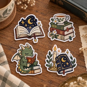 May include: Four embroidered patches featuring literary and fantasy themes. One shows an open book with a night sky, one a stack of books with a teacup, one a green dragon reading a book, and one a candle beside a closed book with a moon.