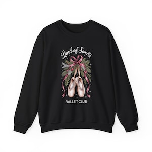 May include: A black long-sleeve sweatshirt featuring a graphic print of two ballet slippers tied with a pink ribbon, surrounded by pine branches and red berries. The text "Land of Sweets" is printed above the slippers and "BALLET CLUB" below.